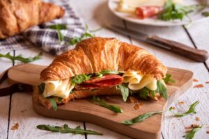 Croissant,Sandwich,With,Cheese,,Meat,And,Arugola,On,White,Wooden